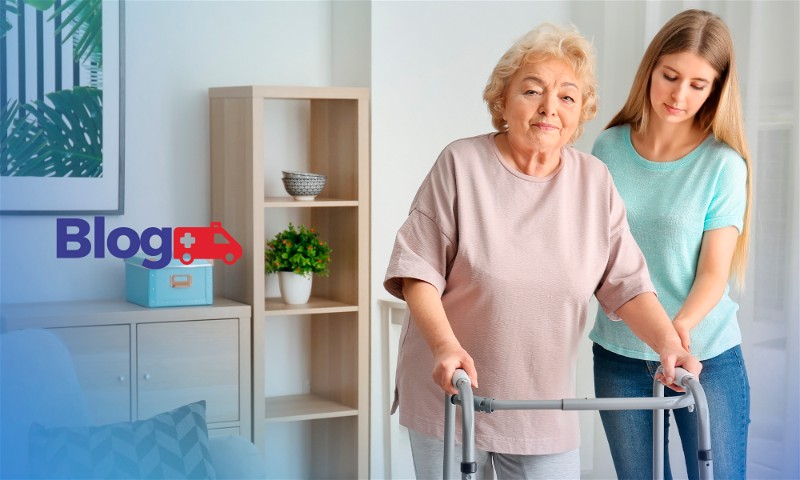 Banner com mulher idoso andando com ajuda de andador acompanhada por mulher, dentro de uma casa