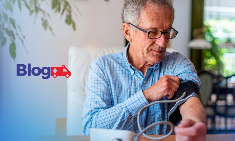 Homem idoso sentado em poltrona aferindo sua pressão com aparelho digital